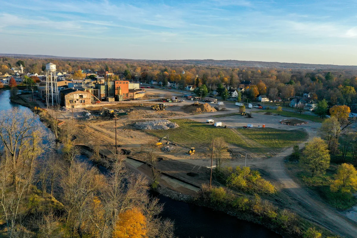 Fall drone view of the cleared mill site, the remaining brick buildings and the water tower beside the river