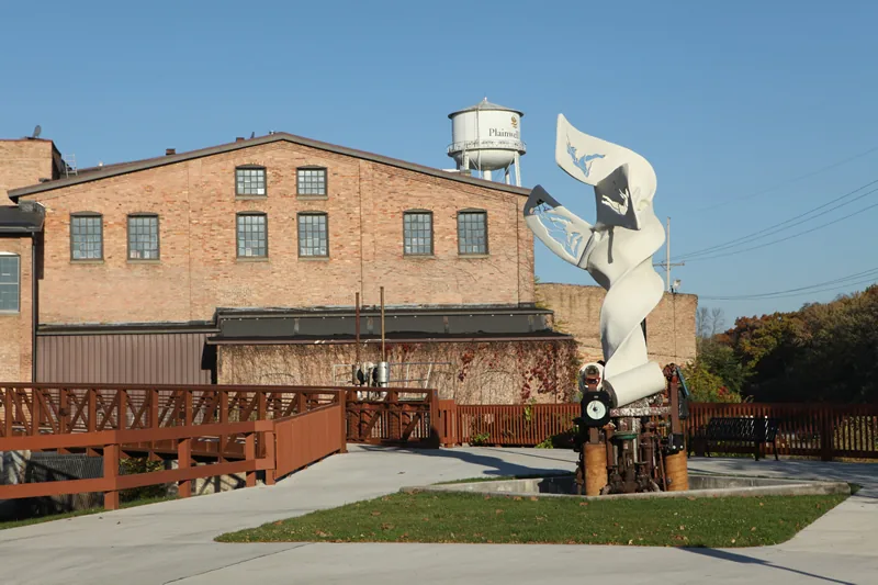 The renovated brick mill building, the water tower and a white sculpture by the river walk